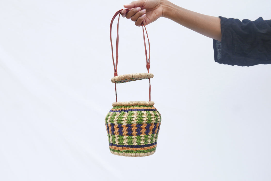 The multicolored Alobahe handbag is handwoven with straw called Kinkahe in Sherigu, Ghana. The shape is versatile and opens from the lid lifted vertical with an adjustable leather strap that can be worn as a crossbody or a handheld bag. This product supports a community with employment, educational opportunities for the children and improve the work environment.