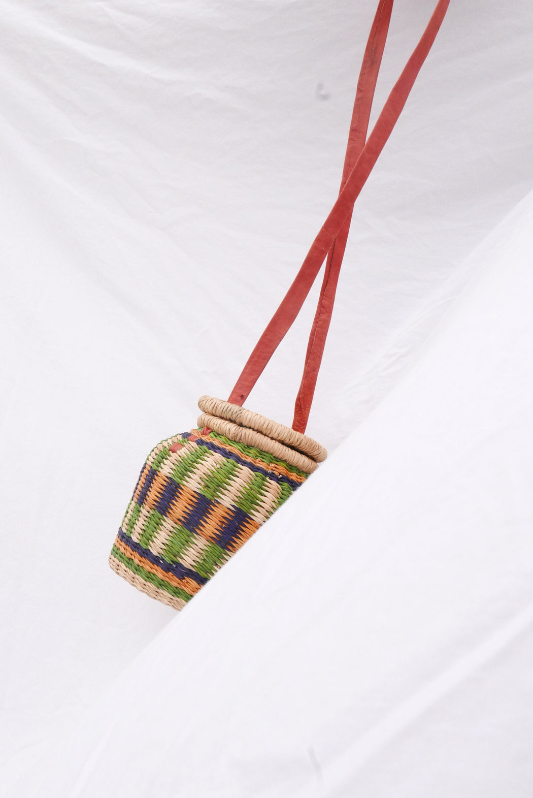 The orange Alobahe handbag is handwoven with straw called Kinkahe in Sherigu, Ghana. The shape is versatile and opens from the lid lifted vertical with an adjustable leather strap that can be worn as a crossbody or a handheld bag. This product supports a community with employment, educational opportunities for the children and improve the work environment.