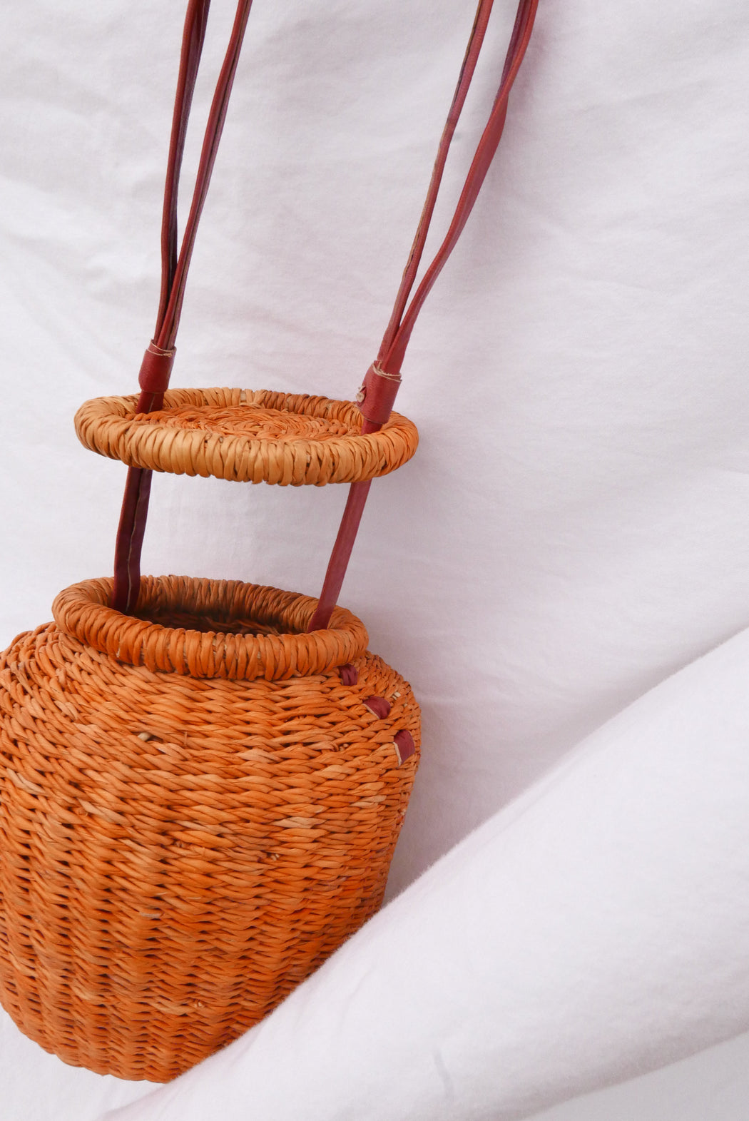 The orange Alobahe handbag is handwoven with straw called Kinkahe in Sherigu, Ghana. The shape is versatile and opens from the lid lifted vertical with an adjustable leather strap that can be worn as a crossbody or a handheld bag. This product supports a community with employment, educational opportunities for the children and improve the work environment.